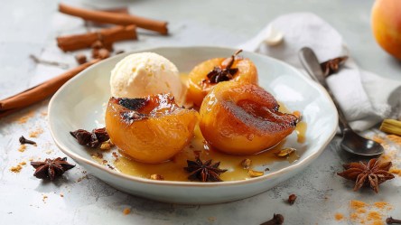 Ein Teller mit gebackenen Gewürz-Quitten mit einer Kugel Vanilleeis. Ringsum liegen Zimtstangen, Sternanis und Nelken herum. Ein Löffel ist zu sehen.
