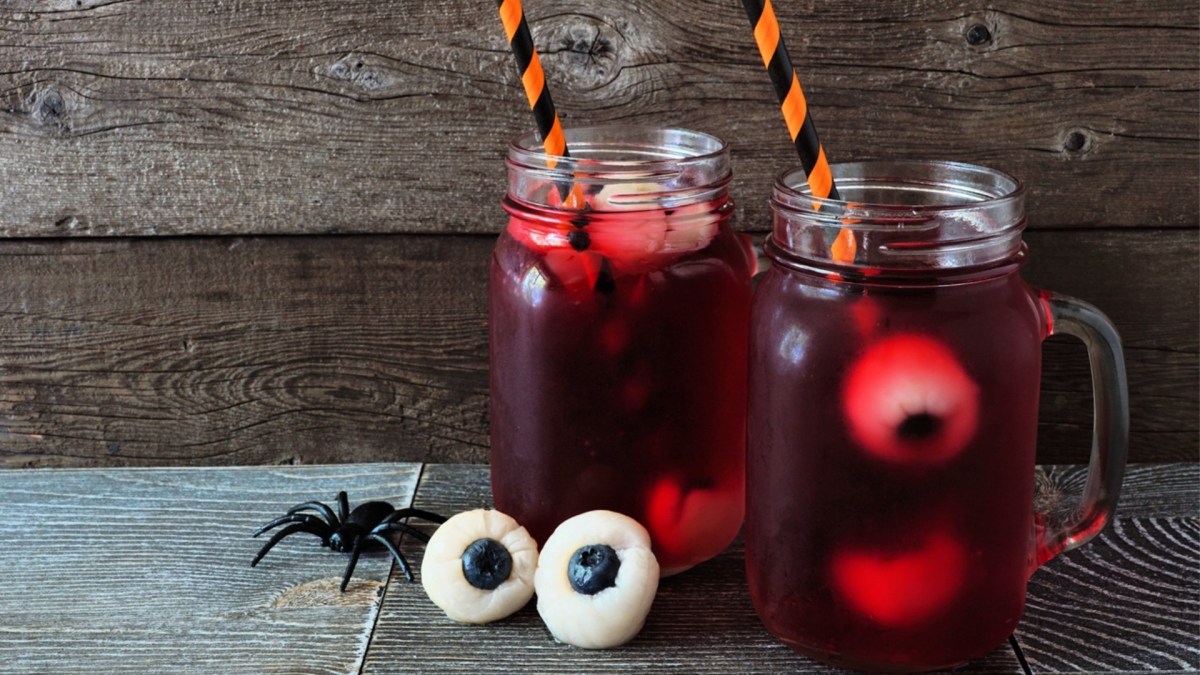 Zwei Gläser mit blutroter Halloween-Bowle ohne Alkohol. Vor den Gläsern liegen zwei Litschi-Heidelbeer-Augen und eine Plastikspinne. Die Getränke sind mit bunten Strohhalmen dekoriert.