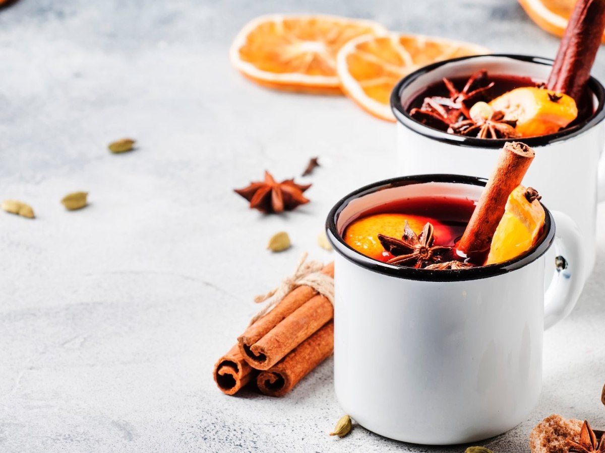 Zwei Tassen Holunderpunsch, garniert mit Zimtstangen, Orangenscheiben und Sternanis.