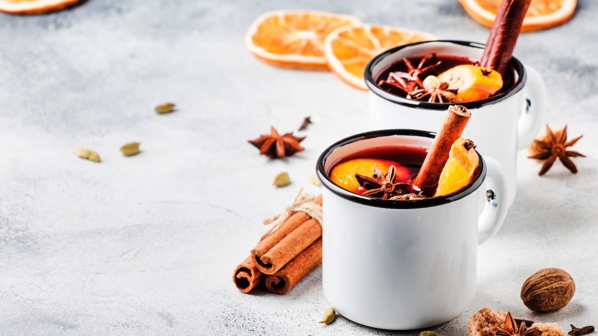 Zwei Tassen Holunderpunsch, garniert mit Zimtstangen, Orangenscheiben und Sternanis.