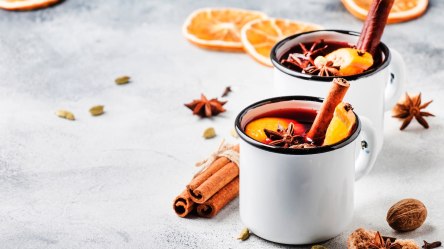 Zwei Tassen Holunderpunsch, garniert mit Zimtstangen, Orangenscheiben und Sternanis.