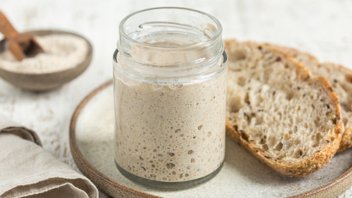 Ist Sauerteig glutenfrei? Ein Glas mit Sauerteigansatz neben einer Scheibe Brot.