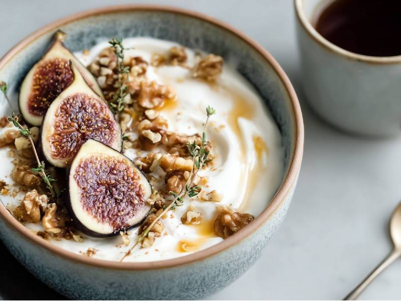 Joghurt-Bowl mit Feigen und Walnüssen, Tasse Kaffee und Löffel daneben