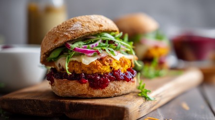 Ein Kürbis-Burger, der auf einem Holzbrett liegt. Im Hintergrund kann man verschwommen einen weiteren Burger erkennen.