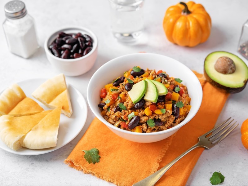 Ein Teller mit Kürbis Hähnchen Chili, garniert mit Avocadospalten. Bunte Deko außen herum.