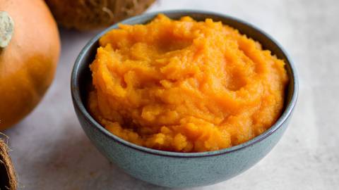 Schale mit Kürbis-Kokos-Püree, Kürbis und Kokosnuss im Hintergrund