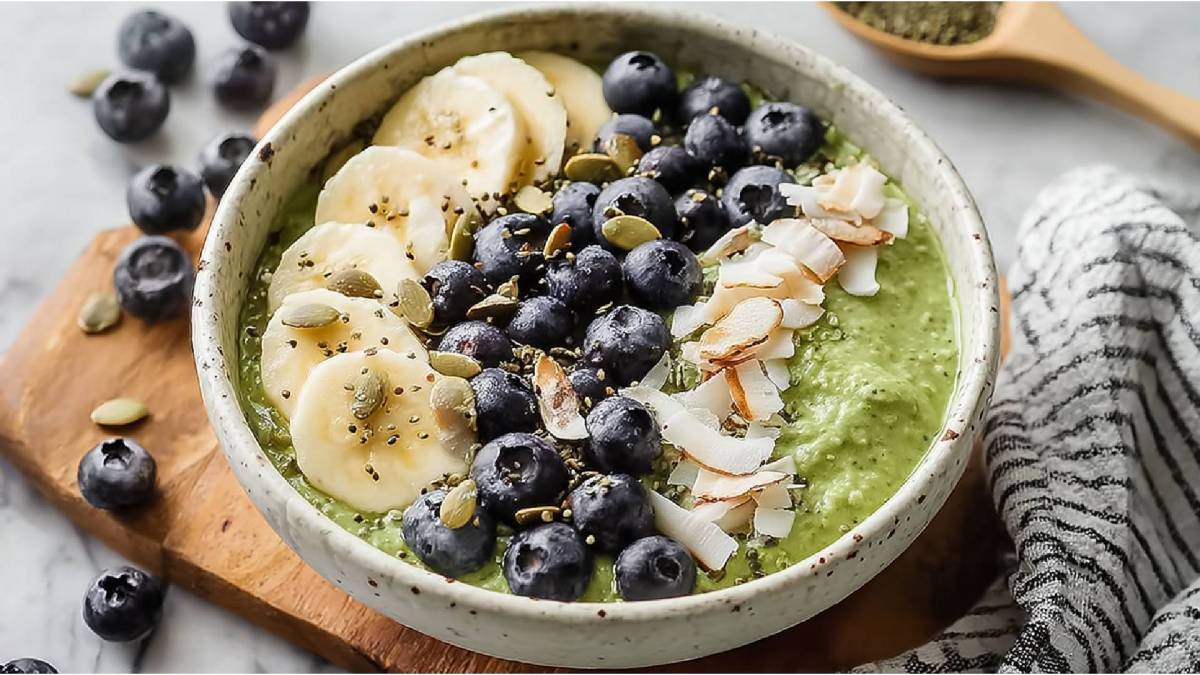 Schale mit Matcha-Overnight-Oats mit Kokos, Bananenscheiben, Kokoschips, Heidelbeeren und Kürbissamen als Topping