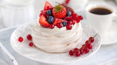 Eine Mini-Pavlova mit Beeren. Daneben steht eine Tasse Kaffee.