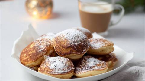 Ein Teller mit mehreren norddeutschen Förtchen mit Puderzucker bestreut und eine Tasse Kaffee im Hintergrund