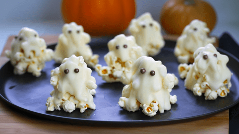 Ein Teller mit Popcorn-Geistern. Zwei Kürbisse sind im Hintergrund zu sehen.