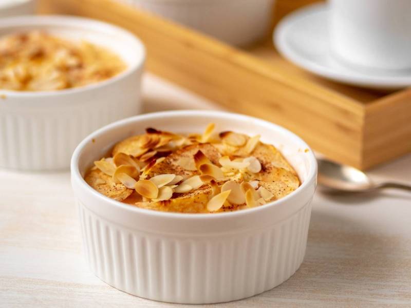 Eine kleine runde Form mit Quark-Grießauflauf mit Äpfeln. Im Hintergrund steht nochmal eine kleine Form sowie ein Tablett mit einer Kaffeetasse.