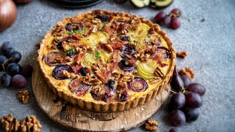 Ein Holzbrett mit Quiche mit Spitzkohl, Trauben und Nüssen. Einige Trauben liegen als Deko außen herum.