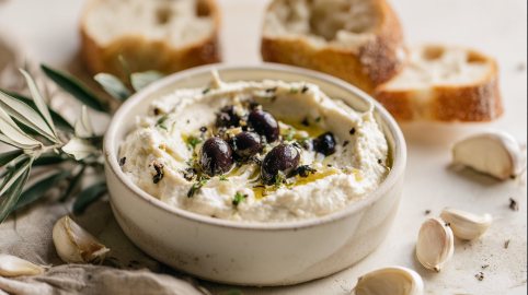 Eine Schüssel Ricotta-Dip mit geröstetem Knoblauch und Oliven.