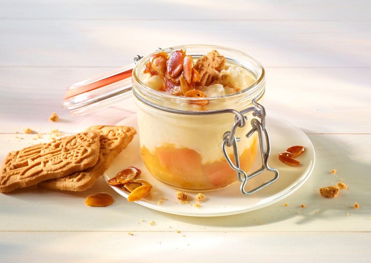 Ein geöffnetes Weckglas gefüllt mit Spekulatius-Milchreis und einer Fruchtschicht. Dekoriert mit Spekulatius-Splittern. Das Glas steht auf einer Untertasse.