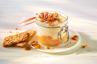 Ein geöffnetes Weckglas gefüllt mit Spekulatius-Milchreis und einer Fruchtschicht. Dekoriert mit Spekulatius-Splittern. Das Glas steht auf einer Untertasse.