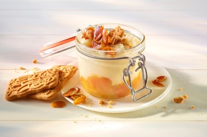 Ein geöffnetes Weckglas gefüllt mit Spekulatius-Milchreis und einer Fruchtschicht. Dekoriert mit Spekulatius-Splittern. Das Glas steht auf einer Untertasse.