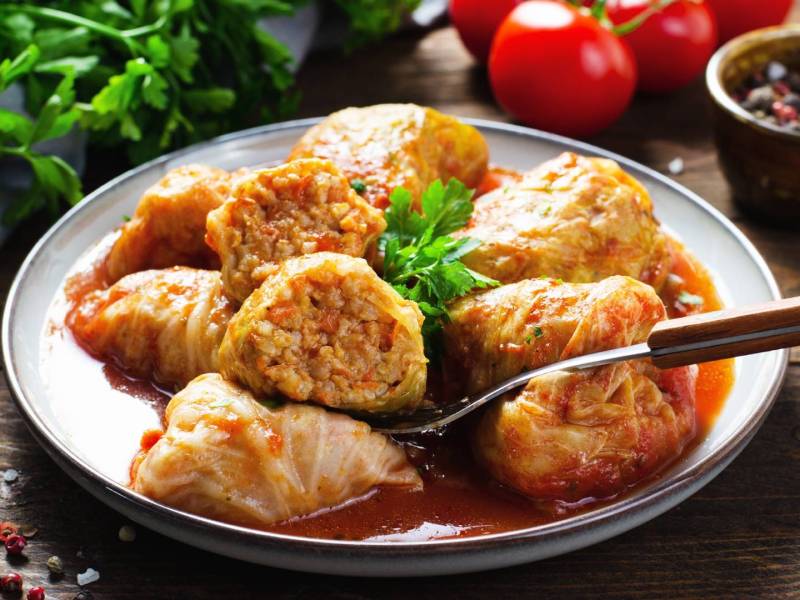 Ein Teller mit ungarischen Kohlrouladen. Im Hintergrund liegen frische Zutaten herum.