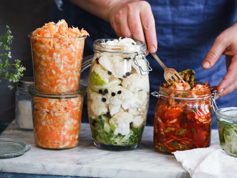 Zero-Waste-Fermentation: Eine Person füllt Gemüse in Einmachgläser.