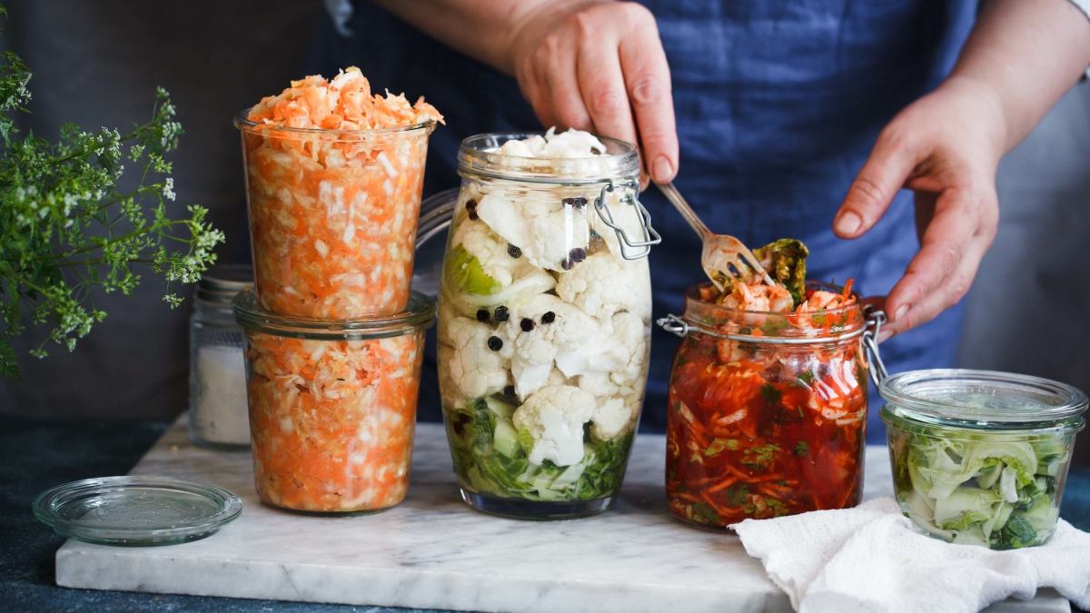 Zero-Waste-Fermentation: Eine Person füllt Gemüse in Einmachgläser.