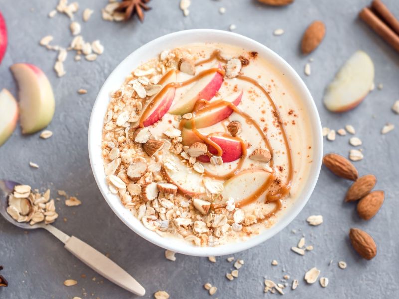 Eine Schale Apple-Crumble-Grießbrei, daneben Gewürze und Äpfel.