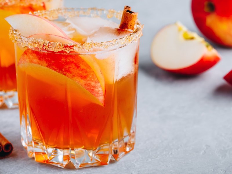 Mehrere Gläser mit Autumn Glow Cocktail, garniert mit Zimtstangen und Apfelspalten.