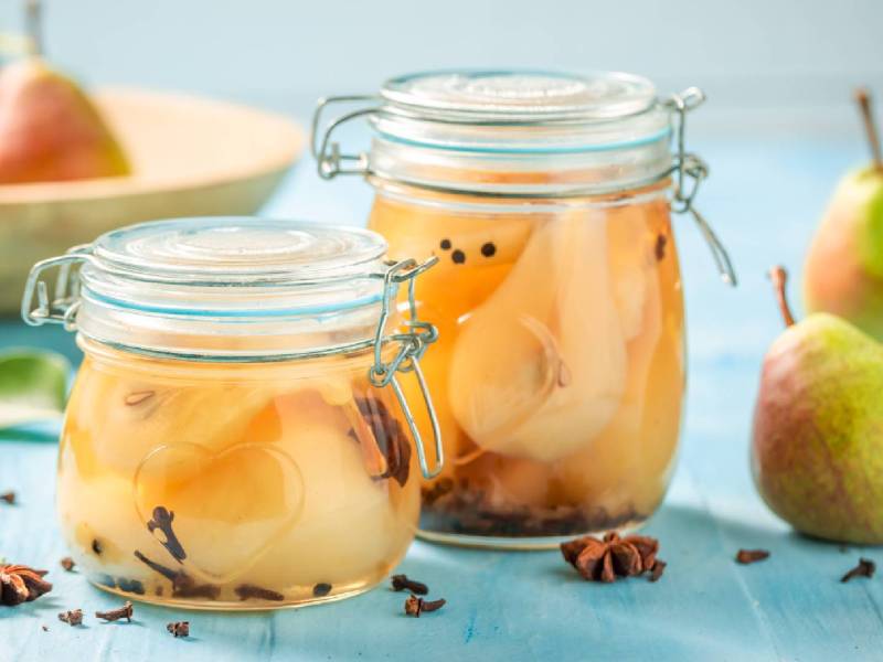 Zwei Gläser mit eingekochten Birnen und frischen Birnen daneben
