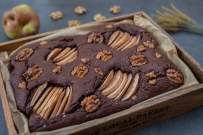 Ein Blech mit Birnen-Walnuss-Brownies. Eine Birne liegt im Hintergrund.