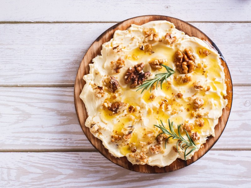 Ein Holzbrett mit Butter mit karamellisierten Walnüssen, Honig und Rosmarin.