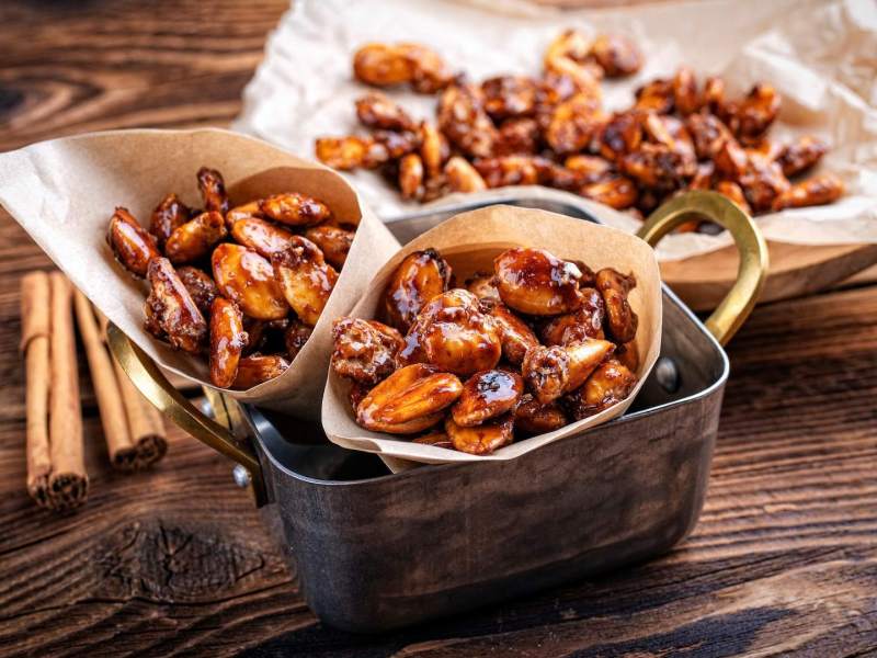 Gebrannte Mandeln in mehreren Tüten auf einem Holzhintergrund.