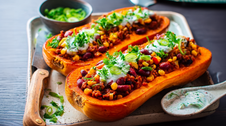 Ein Tablette mit zwei Hälften gefüllter Kürbis mit Chili con Carne. Daneben liegt ein Messer und davor ein Schälchen mit Schmand-Dip.