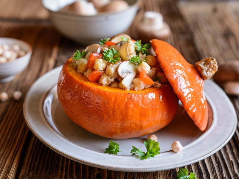 Ein Teller mit gefüllter Kürbis mit Quinoa. Kichererbsen und andere frische Zutaten sind außen herum zu sehen.