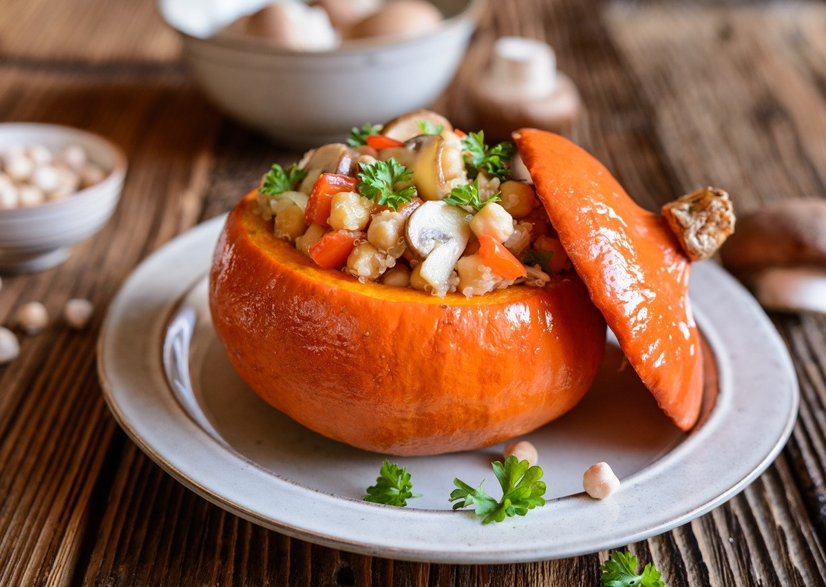 Ein Teller mit gefüllter Kürbis mit Quinoa. Kichererbsen und andere frische Zutaten sind außen herum zu sehen.