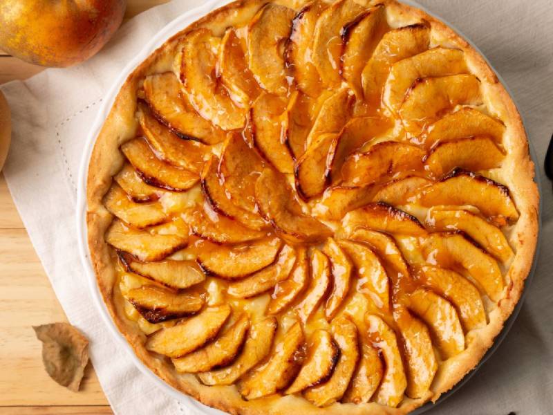 Glasierter Apfelkuchen auf einem Tisch, frische Äpfel daneben
