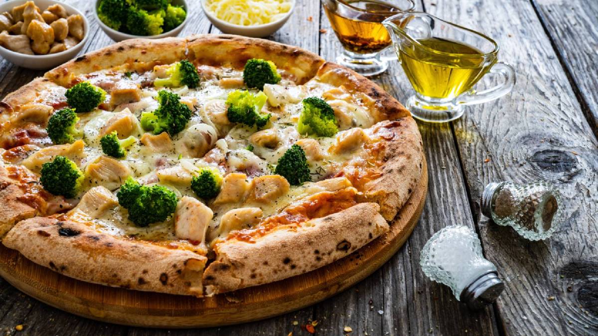 Eine ganze Hähnchen-Brokkoli-Pizza auf einem Tisch, Brokkoli, Olivenöl und Salz daneben