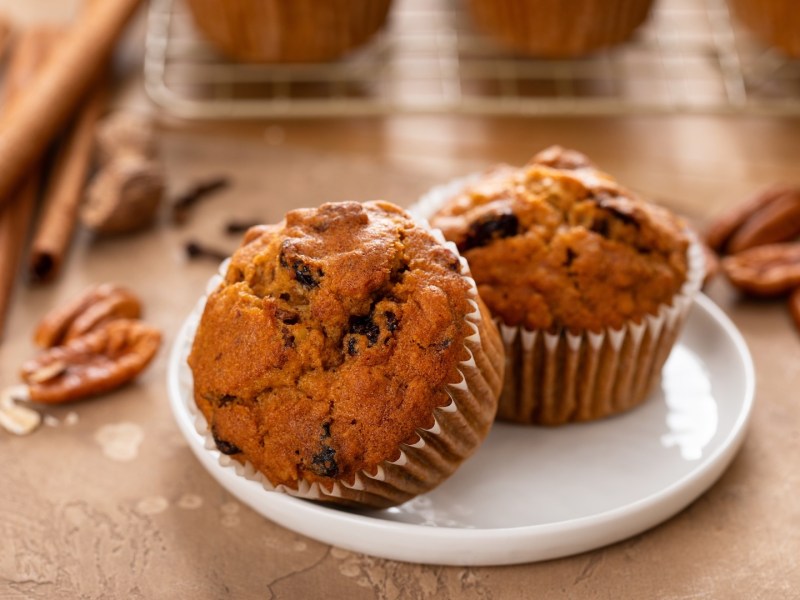 Haferflocken-Gewürz-Muffins auf einem Teller, daneben Zimt und Nüsse.