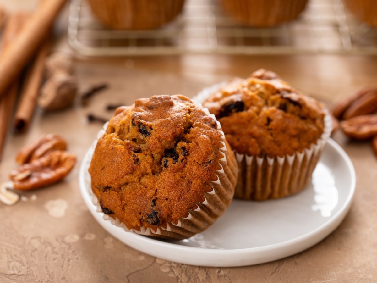 Haferflocken-Gewürz-Muffins auf einem Teller, daneben Zimt und Nüsse.