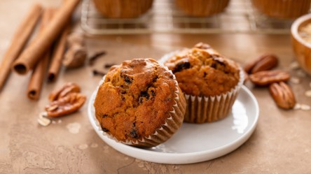 Haferflocken-Gewürz-Muffins auf einem Teller, daneben Zimt und Nüsse.