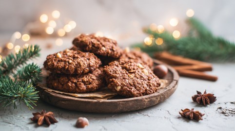 Ein Teller mit Lebkuchen-Haferflockenkeksen. Das Setting ist weihnachtlich mit Tannenzweigen, Zimtstangen, Sternanis und Lichterketten im Hintergrund und um den Teller.