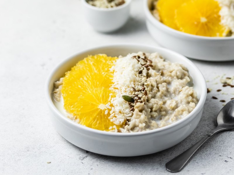 Zwei Schalen Orangen-Porridge, garniert mit Orange und Kernen.