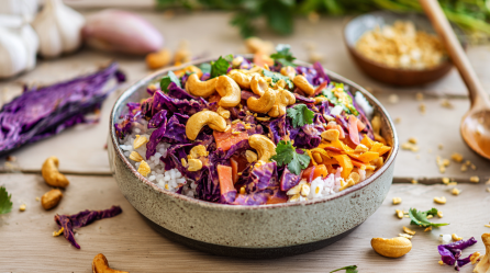 Eine Schale Rotkohl-Curry auf einem Holztisch. Das Curry ist mit Cashewkernen bestreut.