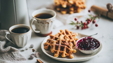 Ein Teller mit Spekulatius-Waffeln mit Glühwein-Kompott. Ringsum kann man zwei Kaffeetassen stehen sehen, sowie winterliche Dekoration und einen Stapel mit Waffeln.