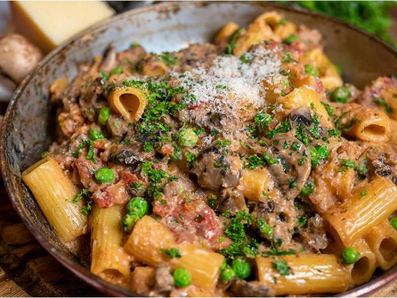 Pfanne mit Südtiroler Hirtennudeln, Champignons und ein Stück Parmesan im Hintergrund