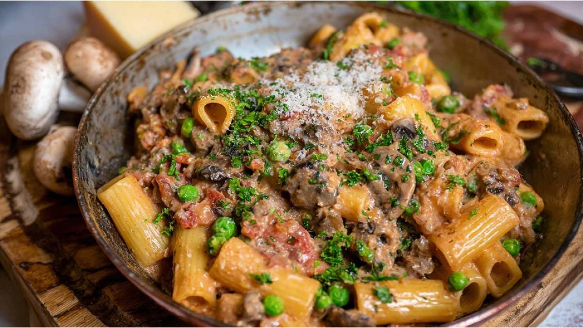 Pfanne mit Südtiroler Hirtennudeln, Champignons und ein Stück Parmesan im Hintergrund
