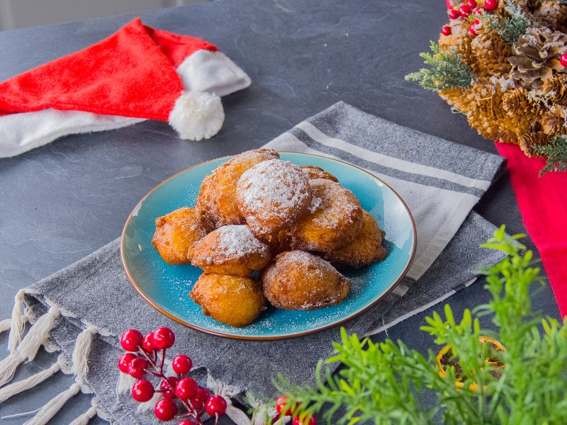 Süße Kartoffelkrapfen auf einem Teller, drum herum weihnachtliche Deko.