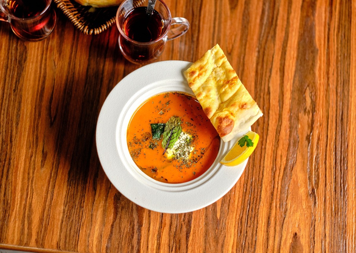 Ein Teller mit türkischer Tarhana-Suppe, garniert mit Kräutern. Ein Stück Fladenbrot liegt am Tellerrand und eine Zitronenspalte.