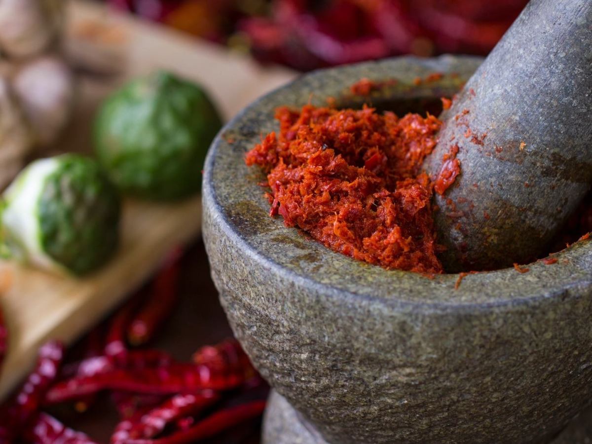 Unterschiede Currypasten: Ein rptes Curry wird in einem Mörser gestampft.