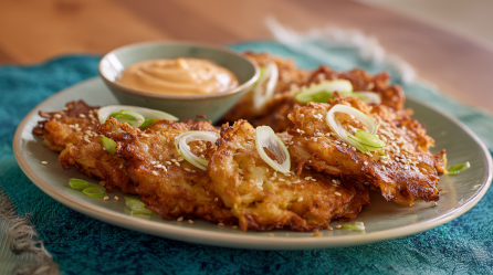Weißkohlpuffer mit Sriracha-Mayonnaise, angerichtet auf einem Teller. Garniert sind die Puffer mit Sesam und Frühlingszwiebeln.