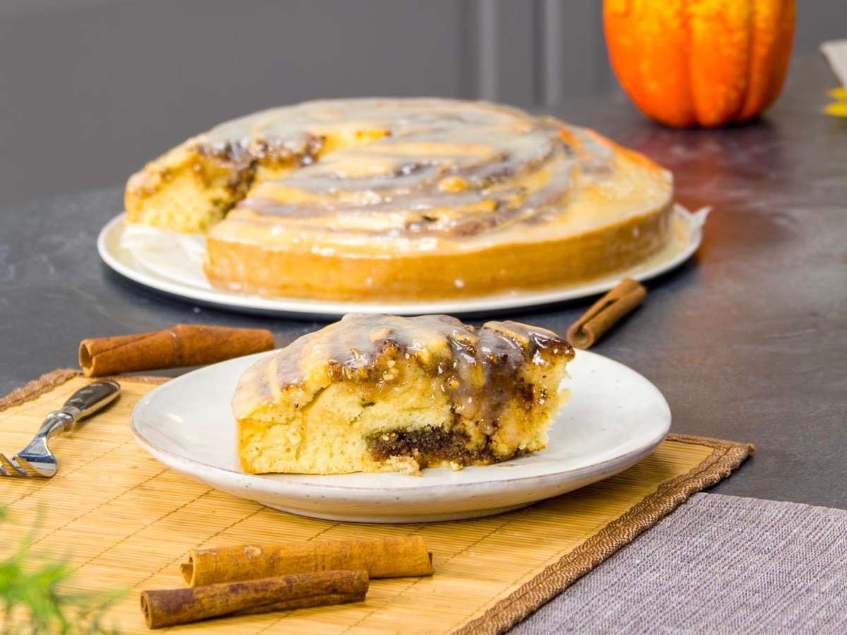 Ein Stück Zimt-Kuchen, der Rest des Kuchens steht im Hintergrund.